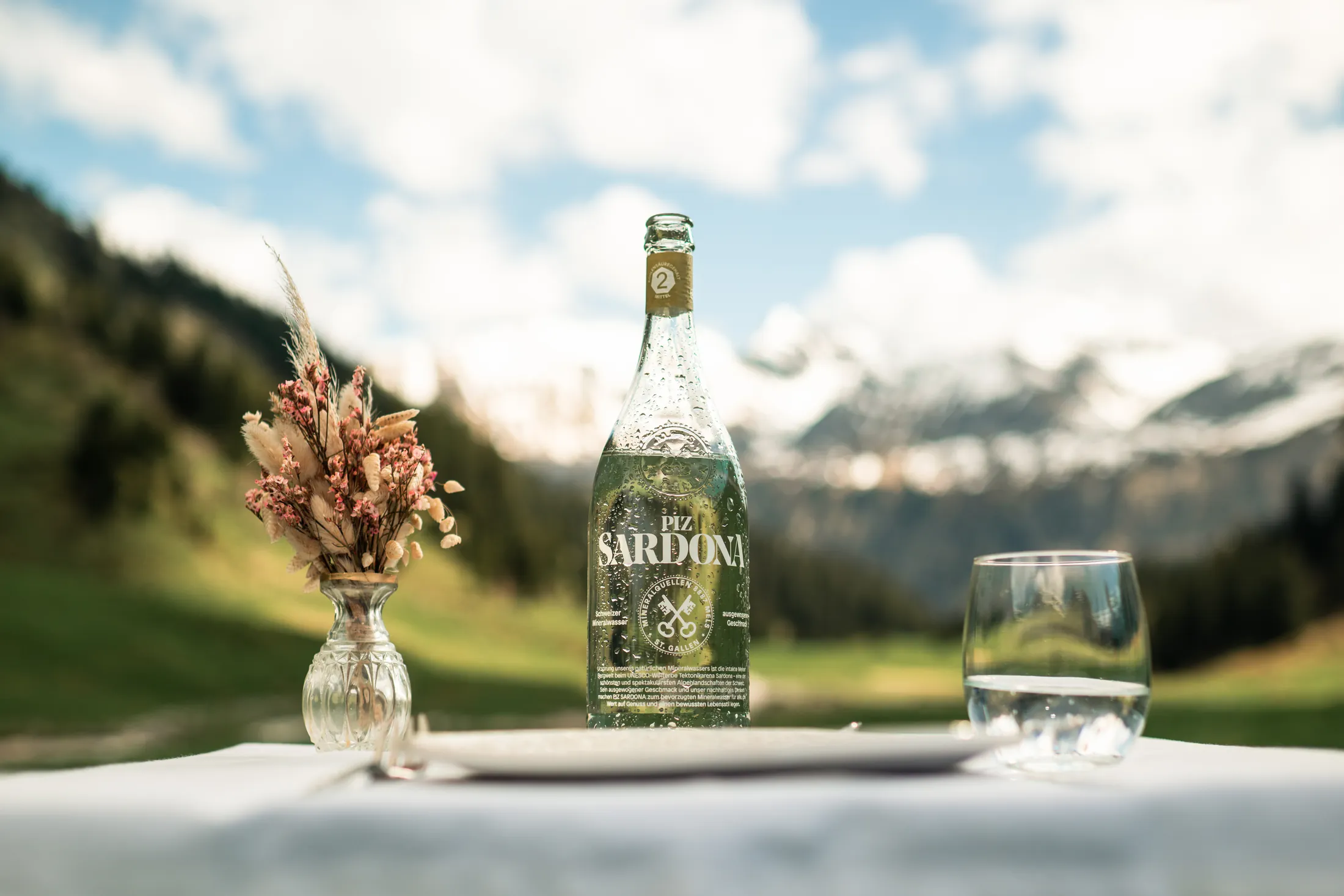 Piz Sardona Flasche auf weissem Tisch vor verschneiten Alpengipfeln